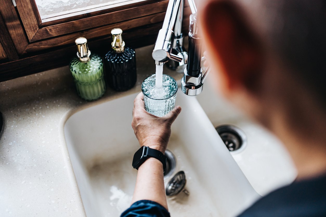 Man getting a glass of water from his kitchen sink - checking water pressure at home.