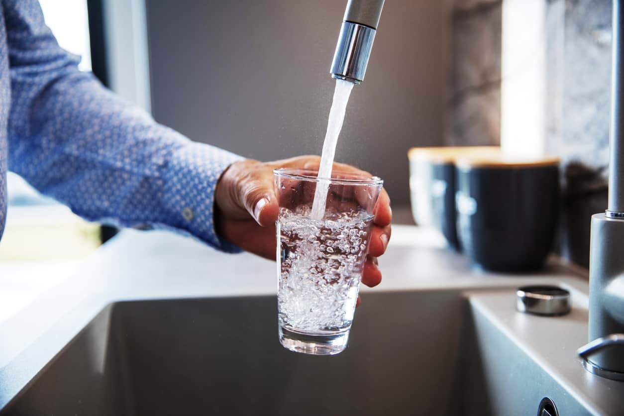 A man filling a glass with water from the tap.