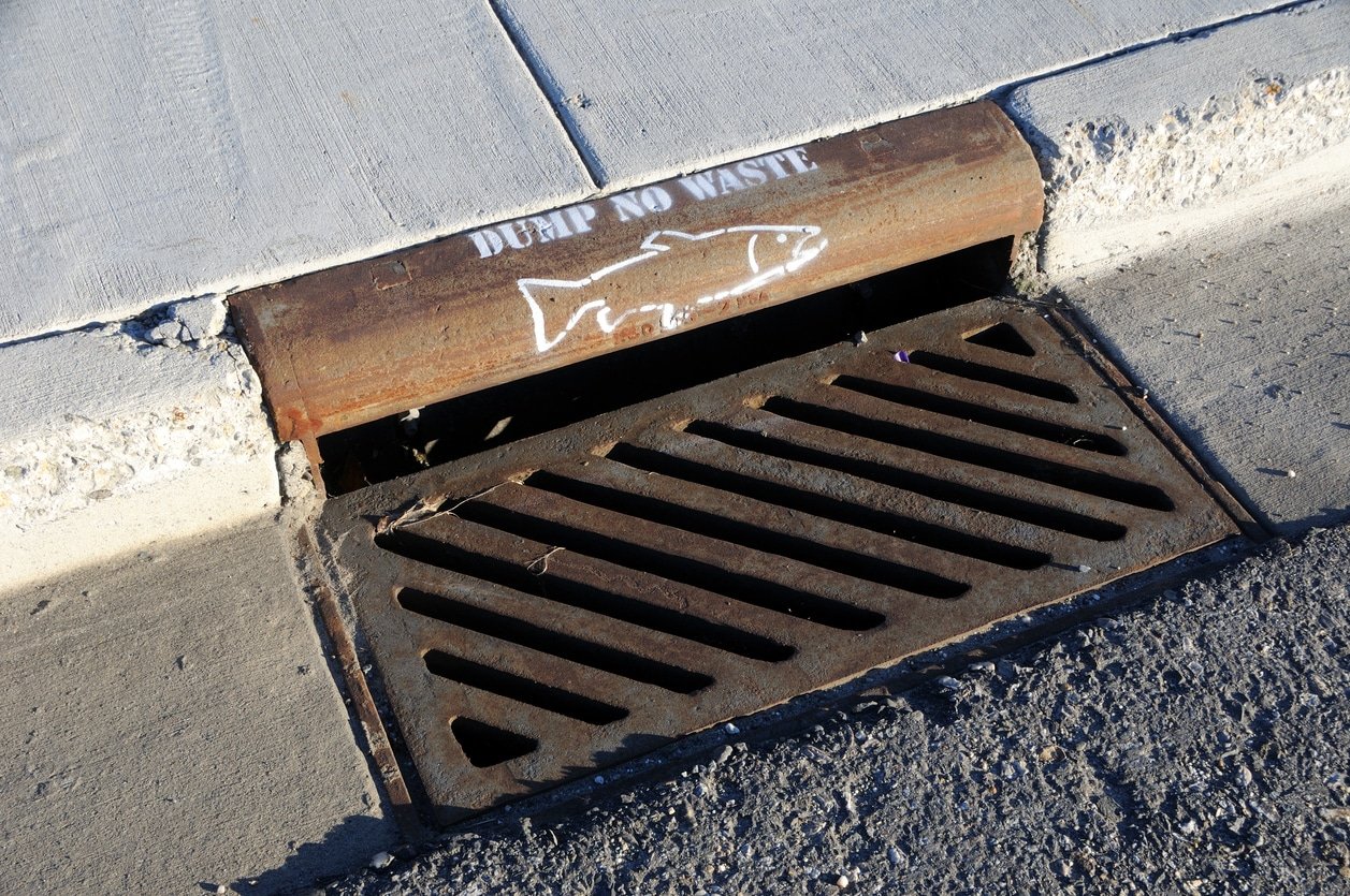 Commercial property's storm drain with installed storm drain traps showing a sign prohibiting the dumping of waste.